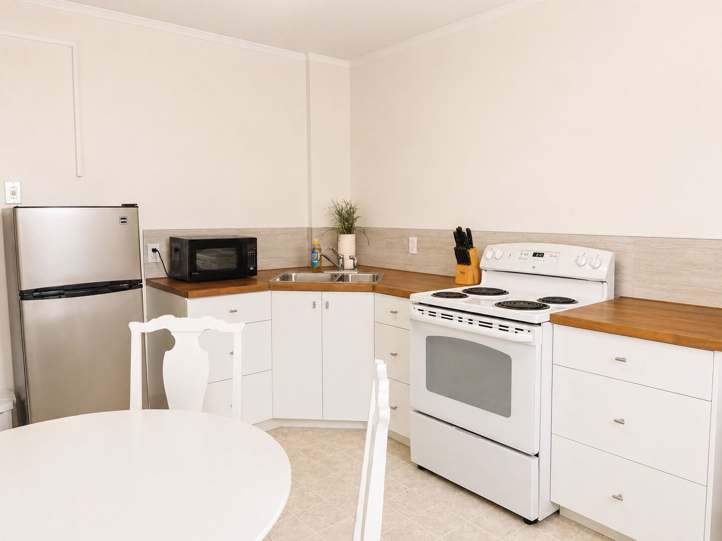 Una cocina con refrigerador, microondas, estufa y gabinetes blancos.