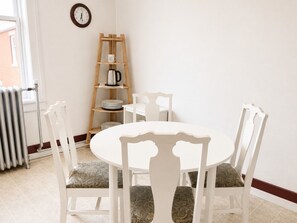A dining area with a round table, white chairs, a wooden shelf with a kettle, and a clock on the wall. - Grand Union Hotel (Coleman)