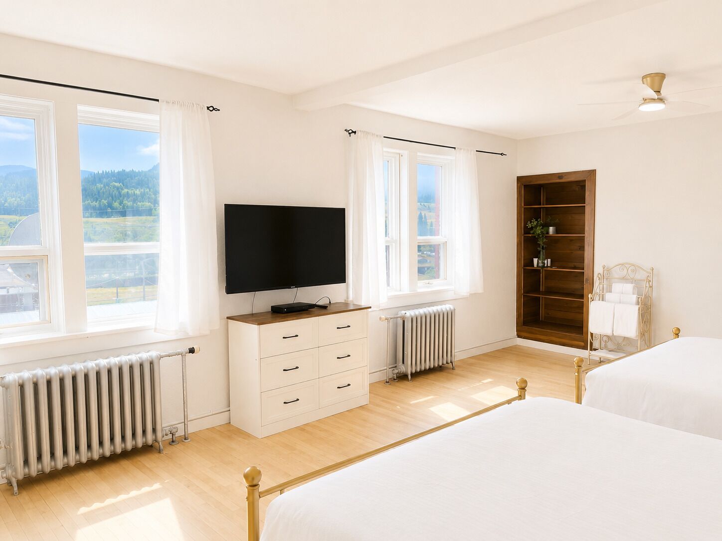 A bedroom with a bed, a TV, a radiator, and a window with curtains.