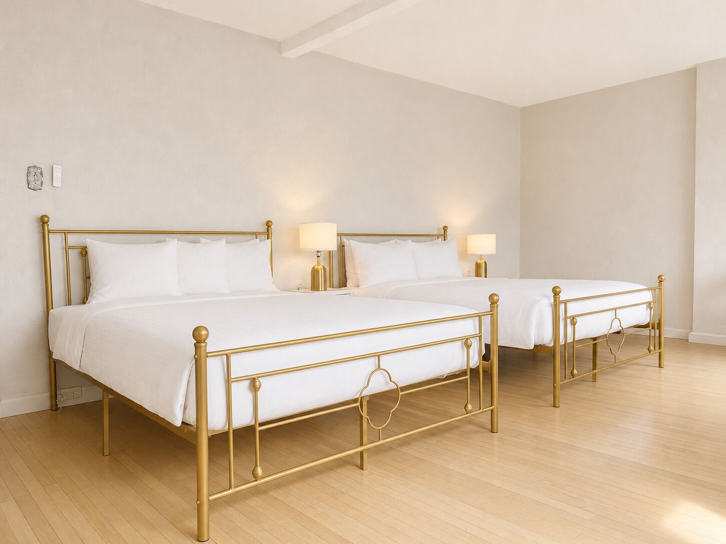 Two twin beds with gold frames in a room with wooden flooring and white walls.