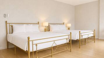Two twin beds with gold frames in a room with wooden flooring and white walls.