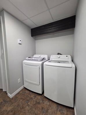 A laundry room with two white front-loading washing machines and a dryer, a white wall, and a tiled floor.