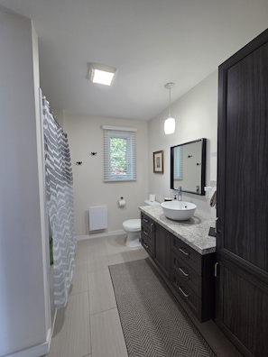 A modern bathroom with a large sink, dark cabinetry, a window with blinds, and a shower curtain.