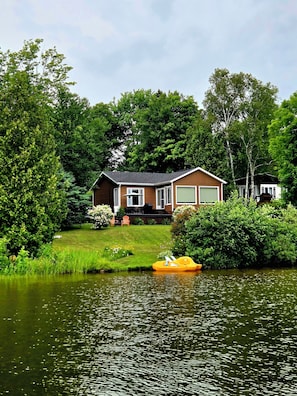 A house with a garage, a lawn, and a small pond with a yellow boat.