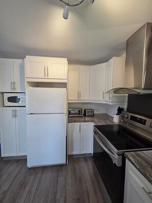 A modern kitchen with white cabinetry, a stainless steel range hood, a microwave, a toaster, and an oven.