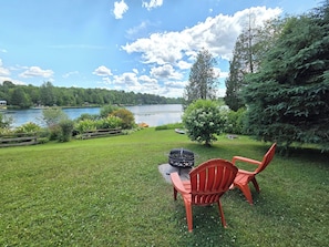 A grassy outdoor area with a lake view, a wooden fence, and a red chair.