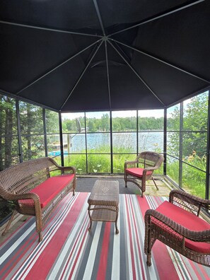 A covered outdoor seating area with wicker furniture and a view of a lake.
