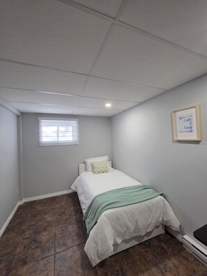 A bedroom with a bed, a window, a wall-mounted picture frame, and a tiled floor.