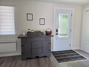 Um quarto com uma cômoda de madeira escura, uma porta branca e uma janela com persianas.