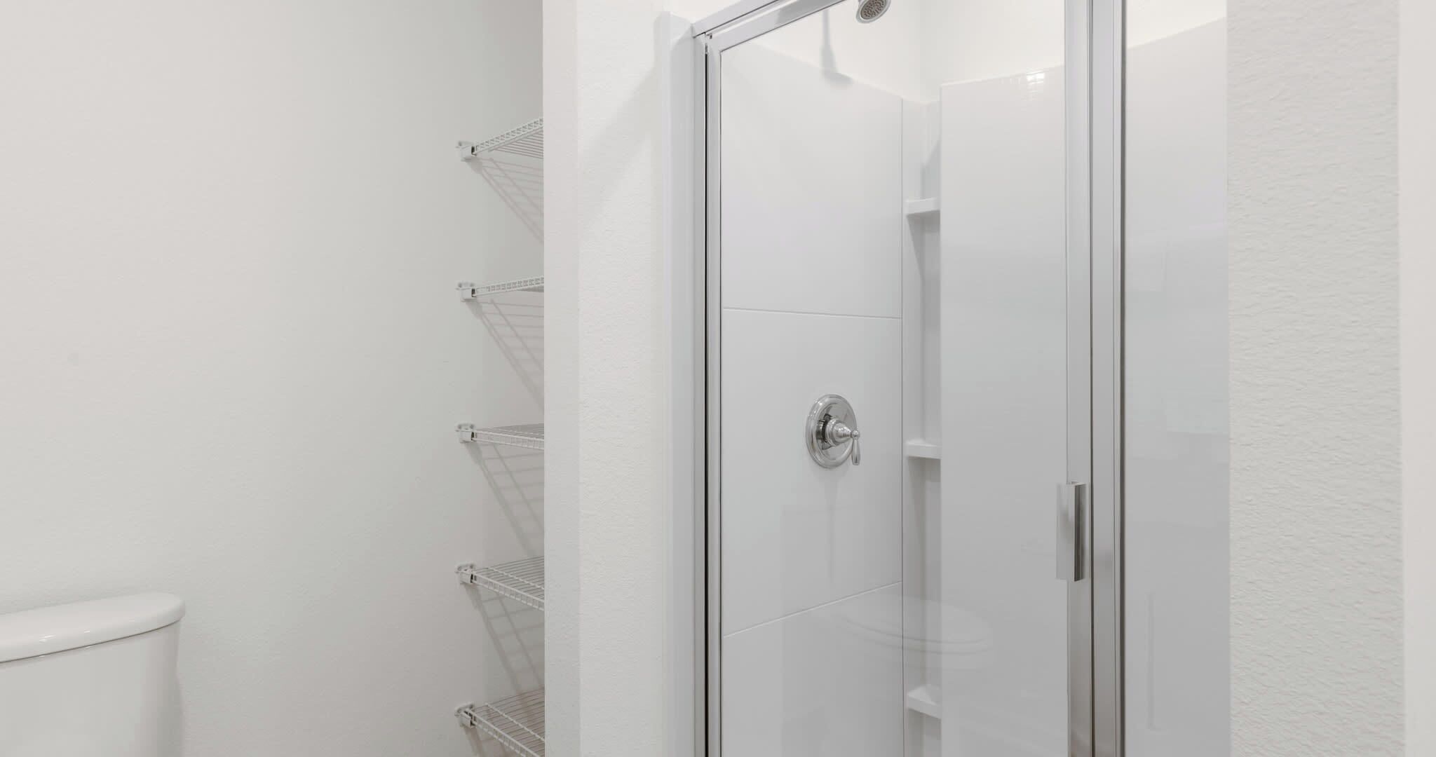 A bathroom with a glass shower enclosure, white walls, and a toilet.