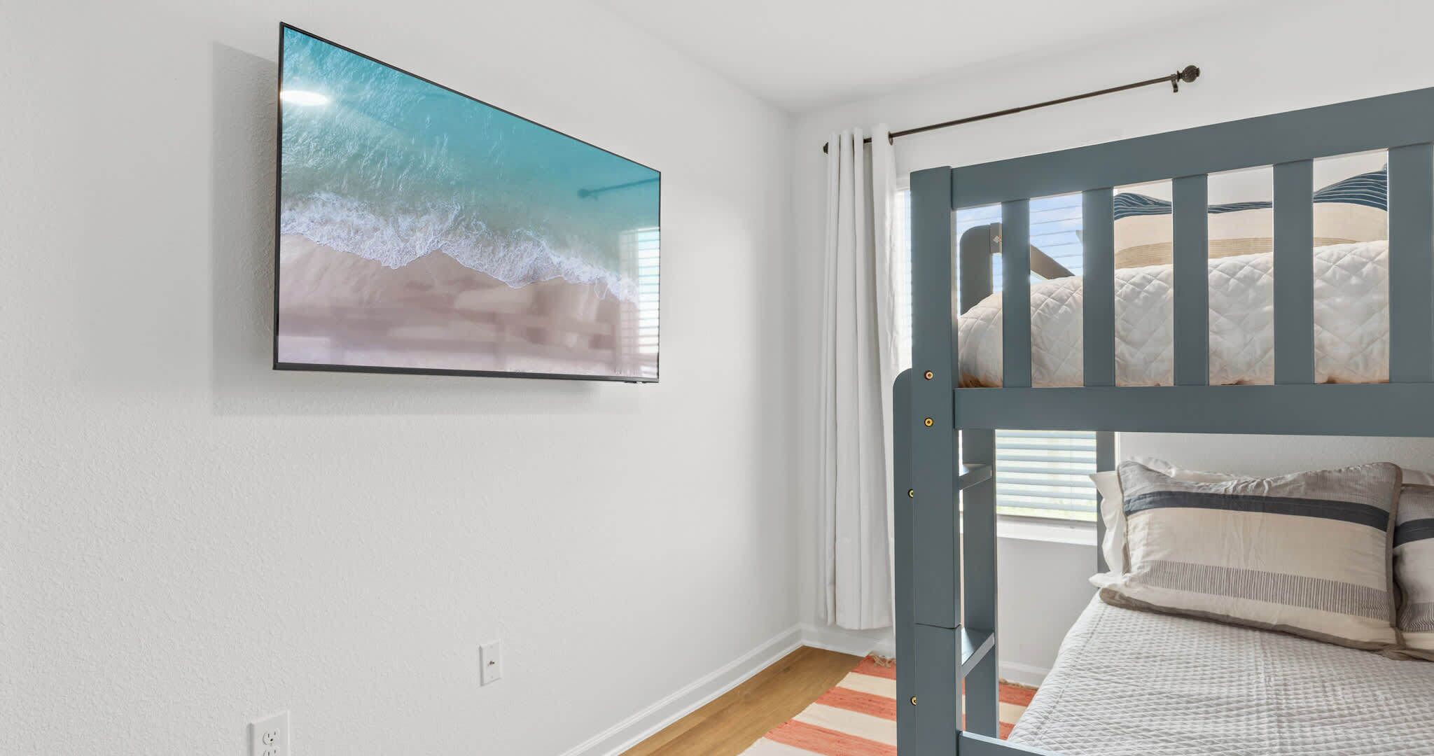A child's bedroom with a bunk bed, a wall-mounted TV, and a window with curtains.