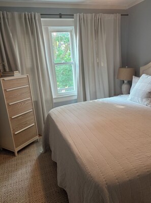 Une chambre à coucher avec un lit, une commode, une fenêtre avec des rideaux et une lampe.