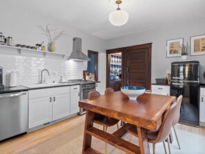 Uma cozinha moderna com armários brancos, uma mesa de jantar de madeira e uma geladeira preta.
