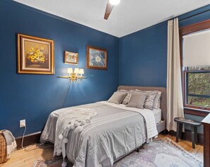 A bedroom with a bed, a nightstand, a lamp, and a window with curtains. - Vintage Art Lodge 4BR/2BA Full Home in Bay View (Milwaukee)