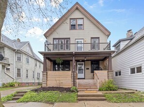 A two-story house with a front porch, a garage, and a small garden area. - Vintage Art Lodge 4BR/2BA Full Home in Bay View (Milwaukee)