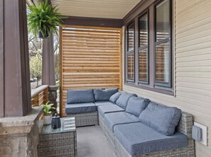 Uma área de estar coberta ao ar livre com um sofá modular e uma mesinha com uma planta.
