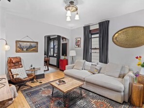 A living room with a sofa, armchair, coffee table, and a rug. There is a painting on the wall and a lamp on a side table. - Vintage Art Lodge 4BR/2BA Full Home in Bay View (Milwaukee)