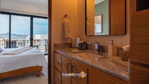 Habitación de hotel con cama, baño con espejo grande y vista a la ciudad.