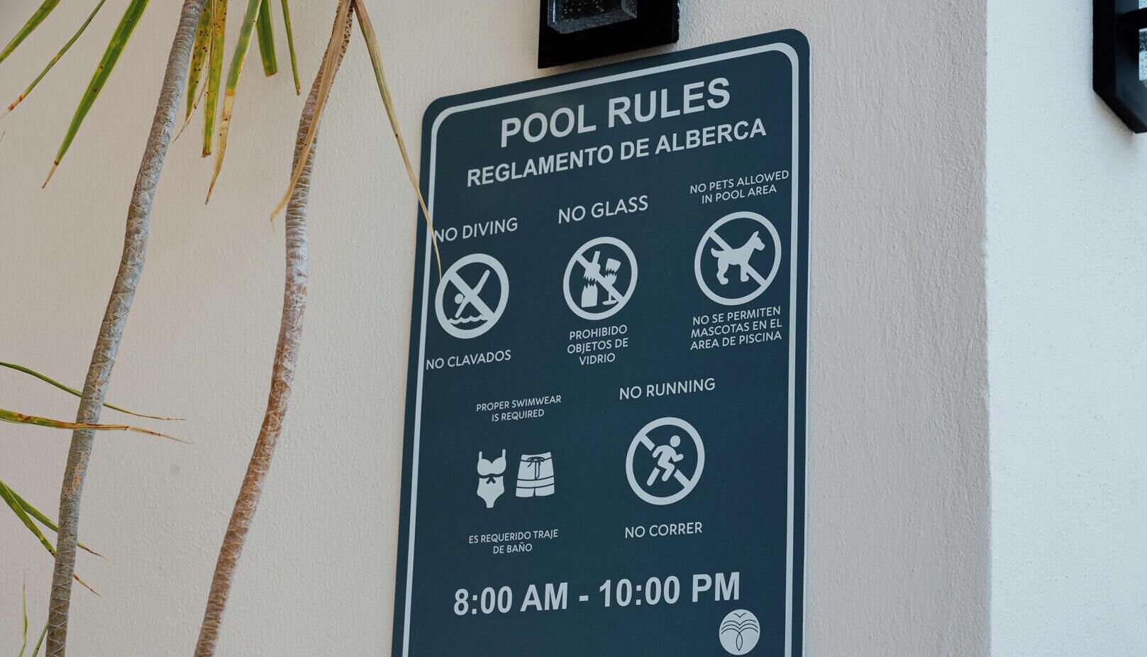 A pool rules sign with regulations such as no diving, no glass, no pets, no running, and proper swimwear required.