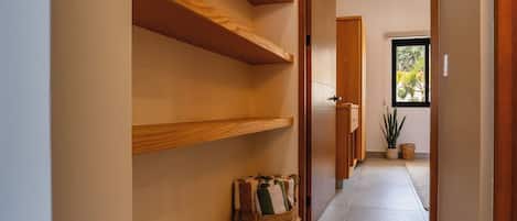 Un pasillo con estantes de madera, una cesta tejida y una puerta que da a una habitación con ventana.