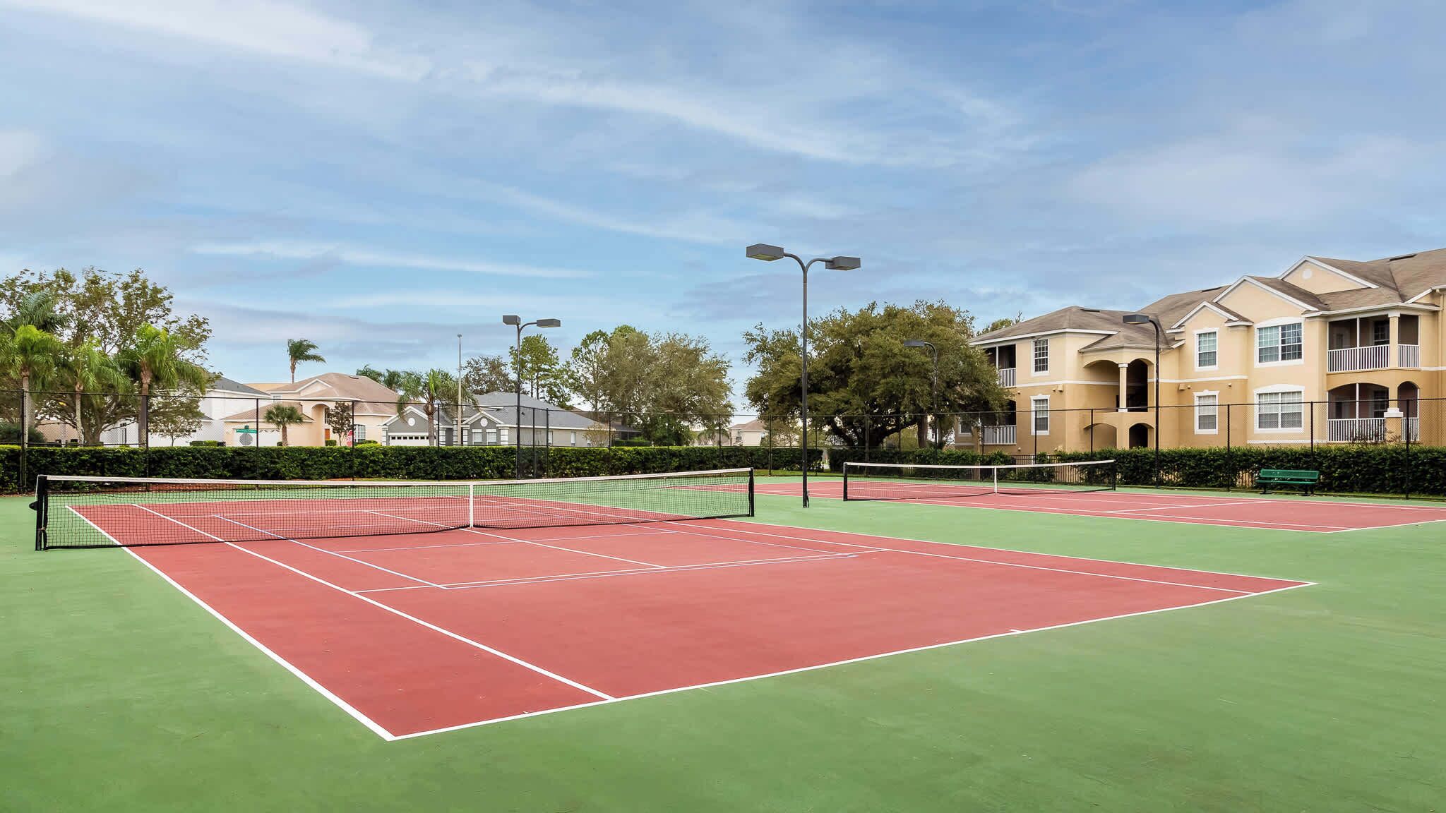 Un court de tennis avec un filet, entouré de verdure et de bâtiments.