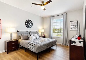 Ein Schlafzimmer mit Bett, Nachttischen, Deckenventilator, Fenster mit Vorhängen und Wanddekoration.