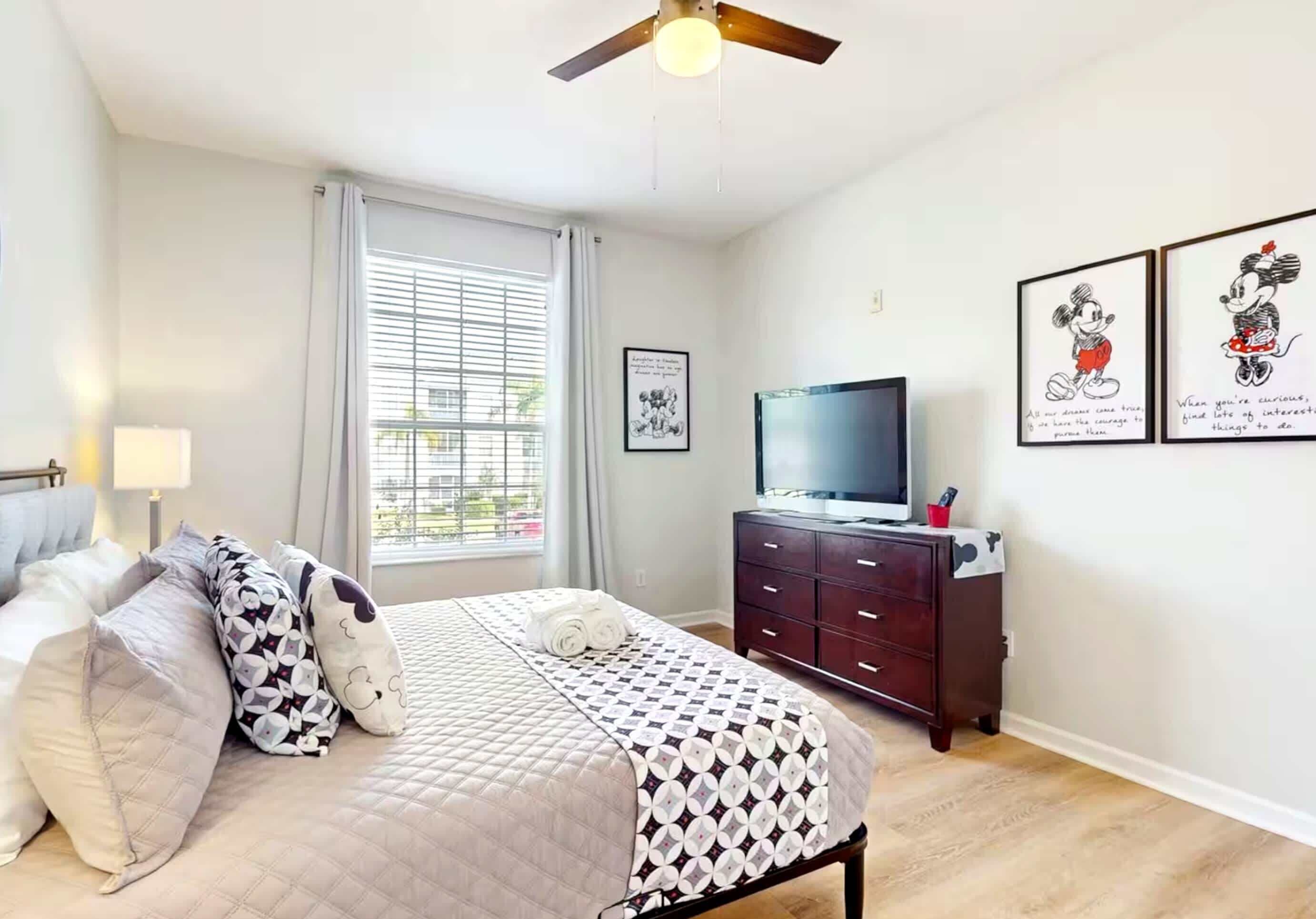 A bedroom with a bed, a TV, a dresser, and a window with blinds.