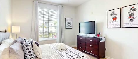 A bedroom with a bed, a TV, a dresser, and a window with blinds.