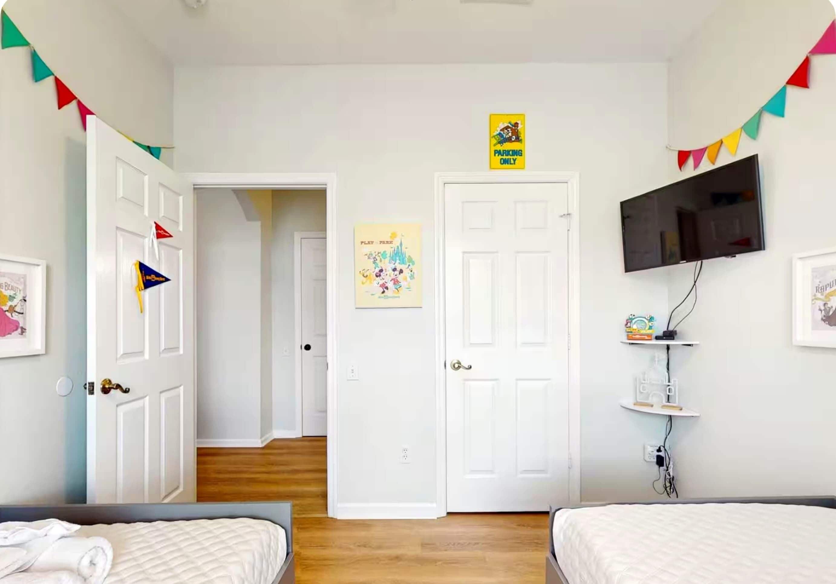 A bedroom with two beds, a TV mounted on the wall, and a door leading to another room.
