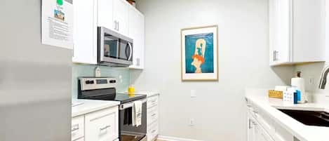 Een moderne keuken met witte kasten, een magnetron, oven en spoelbak. Aan de muur hangt een lijst met een foto en er ligt een klein vloerkleed.