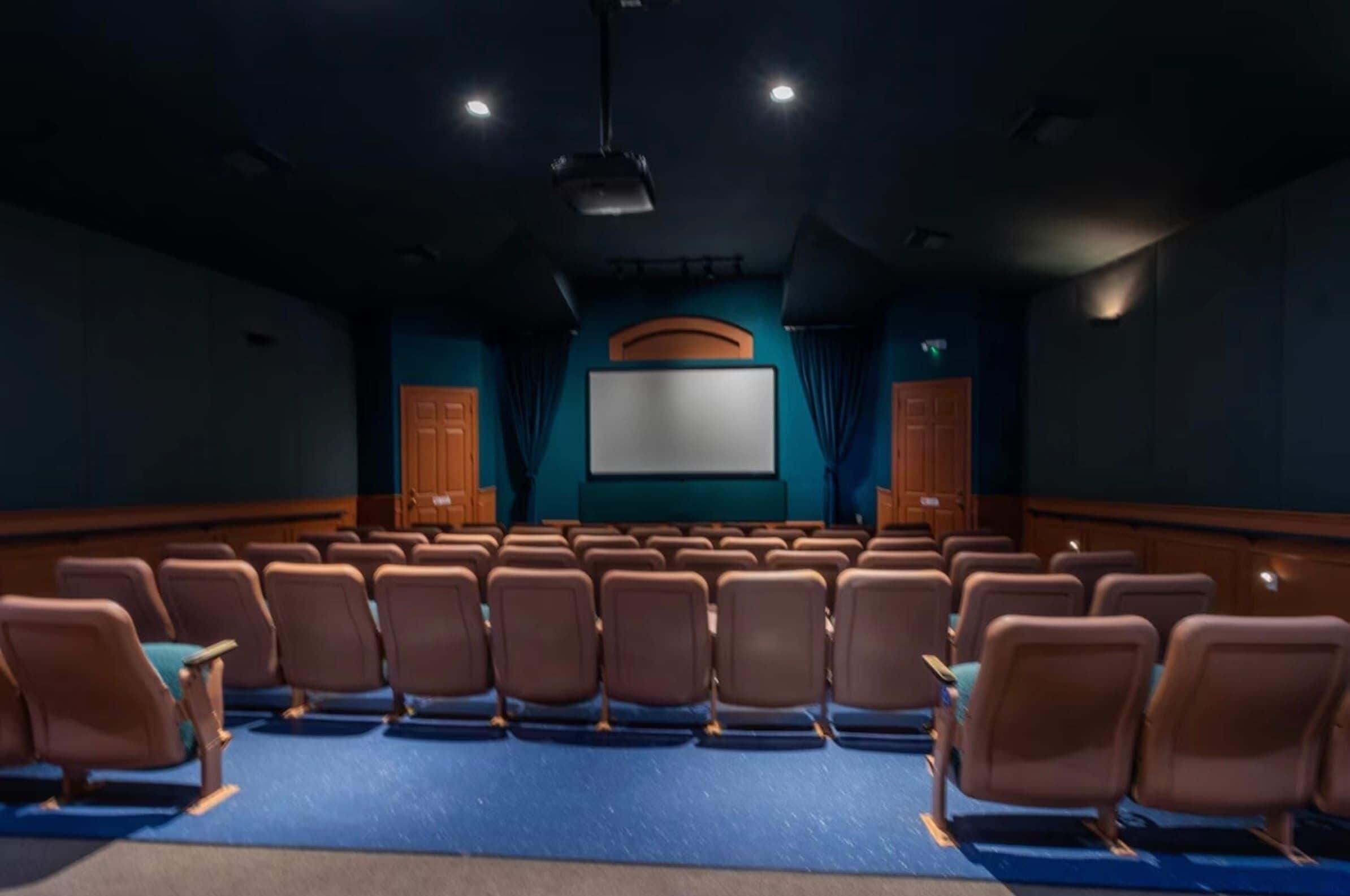 A theater with rows of seats, a large screen, and wooden paneling.