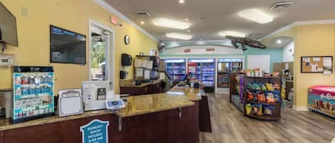 A reception area with a counter, a clock, a vending machine, and a sign indicating sundry shop hours.
