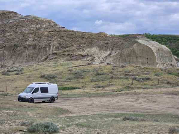 Un fourgon blanc est garé sur un chemin de terre, avec une grande formation rocheuse en arrière-plan.