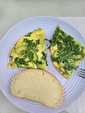 Une assiette avec une tranche de pain grillé garni d’avocat et une tranche d’omelette aux légumes.