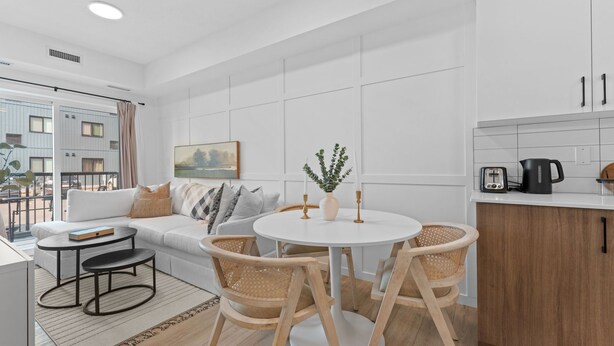 Una sala moderna con un sofá, una mesa de comedor redonda y sillas. Hay una zona de cocina con armarios y un hervidor.