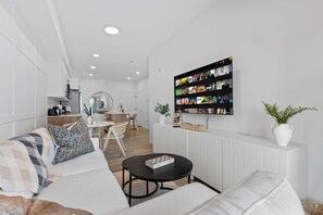 A modern living room with a flat-screen TV mounted on the wall displaying a movie selection. - The Willow | Boutique 1BR w/ Balcony (Edmonton)