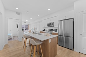 A modern kitchen with a central island, stainless steel appliances, and wooden accents. - The Willow | Boutique 1BR w/ Balcony (Edmonton)