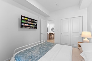 Ett modernt sovrum med en säng, en tv som är monterad på väggen och visar Netflix-gränssnittet, ett sängbord med en lampa och en dörr som leder till ett badrum.