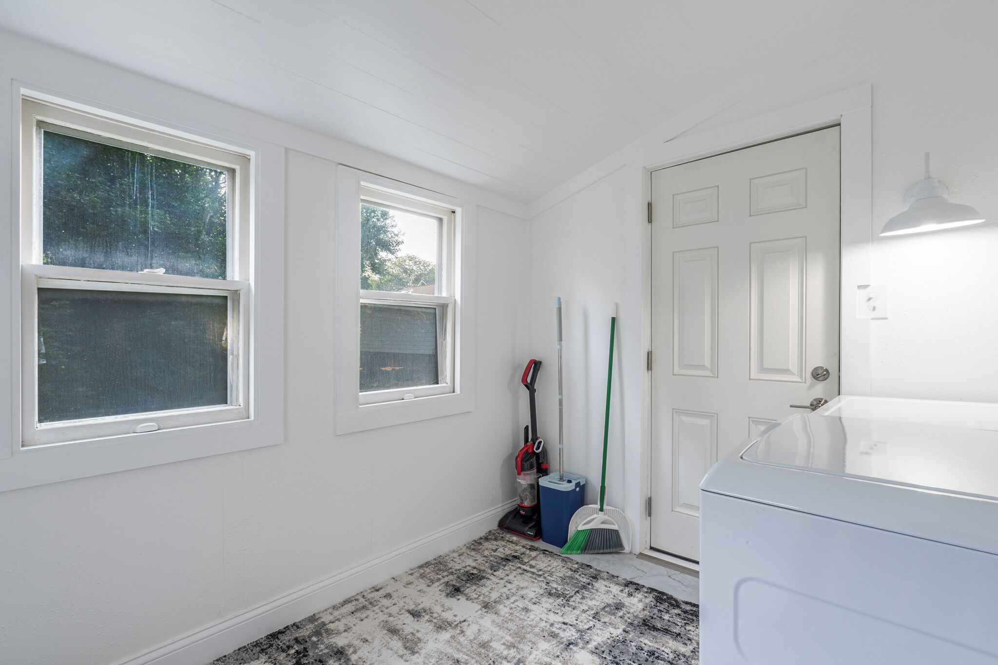 A laundry room with two windows, a door, and a washing machine.
