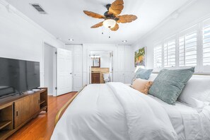Ein Schlafzimmer mit einem Bett, einem Fernseher, einem Deckenventilator und einem durchgehenden Türspalt sichtbaren Badezimmer.