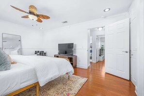 Quarto com cama, televisão, ventoinha no teto e porta que dá para outro espaço.