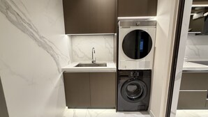 Een kleine wasruimte met een ingebouwde wasmachine en droger, een wasbak en een marmeren achterwand.