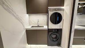 Ein kleiner Waschraum mit integrierter Waschmaschine und Trockner, einem Waschbecken und einer Marmor-Spritzschutzwand.