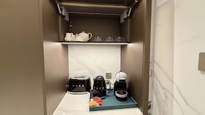 Eine kompakte Küchenzeile mit Toaster, zwei Kaffeemaschinen und einer kleinen Ablage für Tassen und Gläser.