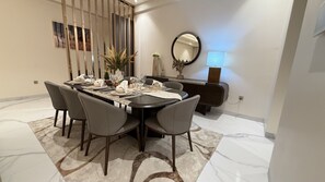 A dining area with a round table set for six, surrounded by chairs, with a decorative plant and a mirror on the wall. - Grand Residence 3 bedroom deluxe appartment with club house (Kinshasa)