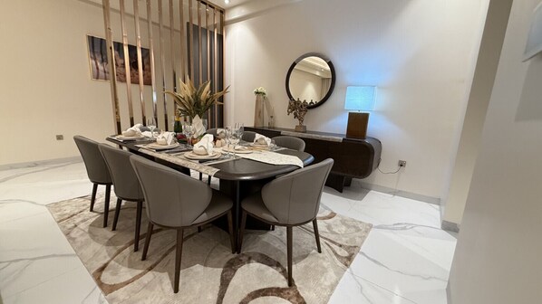 A dining area with a round table set for six, surrounded by chairs, with a decorative plant and a mirror on the wall. - Grand Residence 3 bedroom deluxe appartment with club house (Kinshasa)