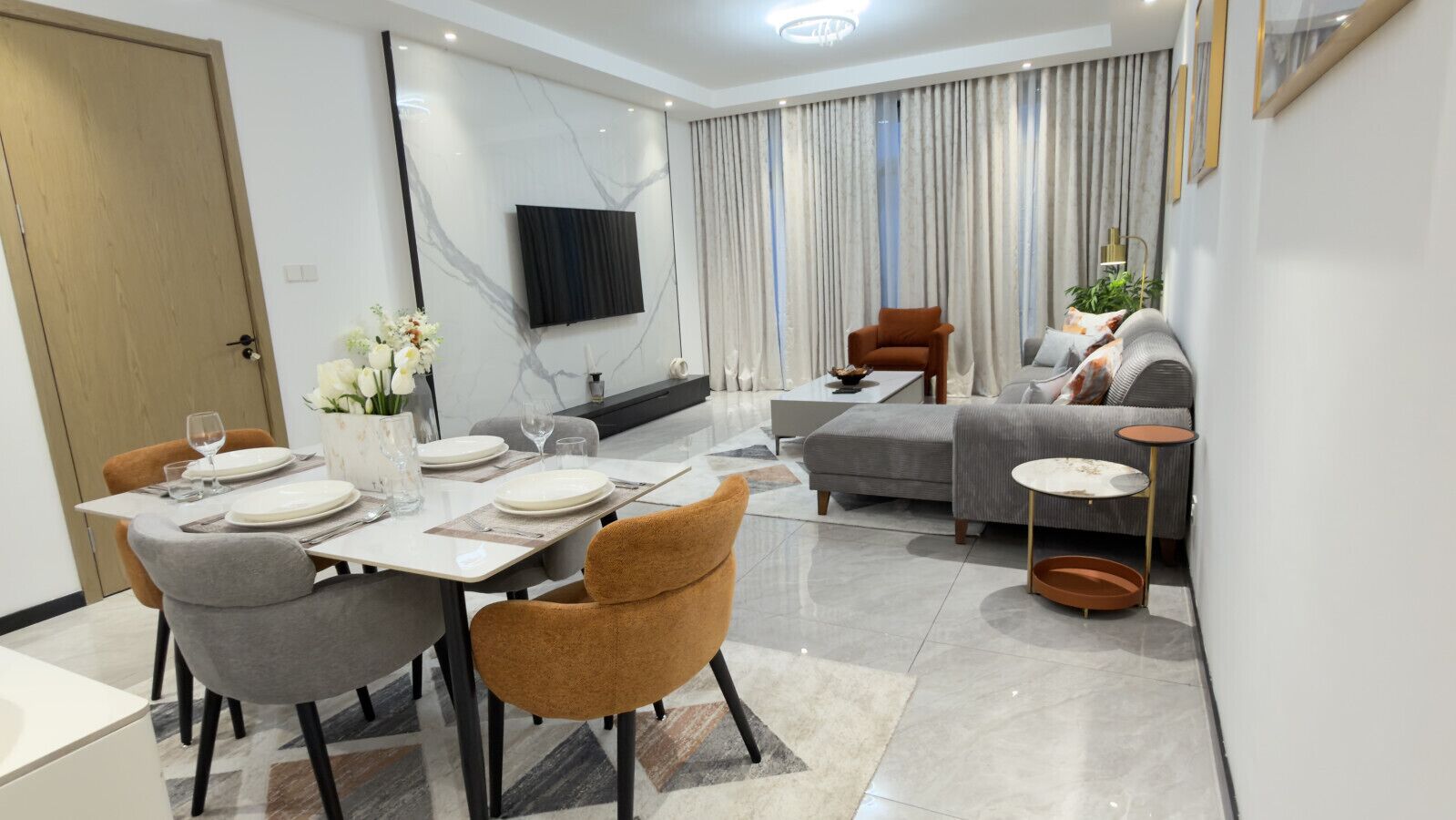 A modern living room with a dining area, a sofa, and a television mounted on the wall.