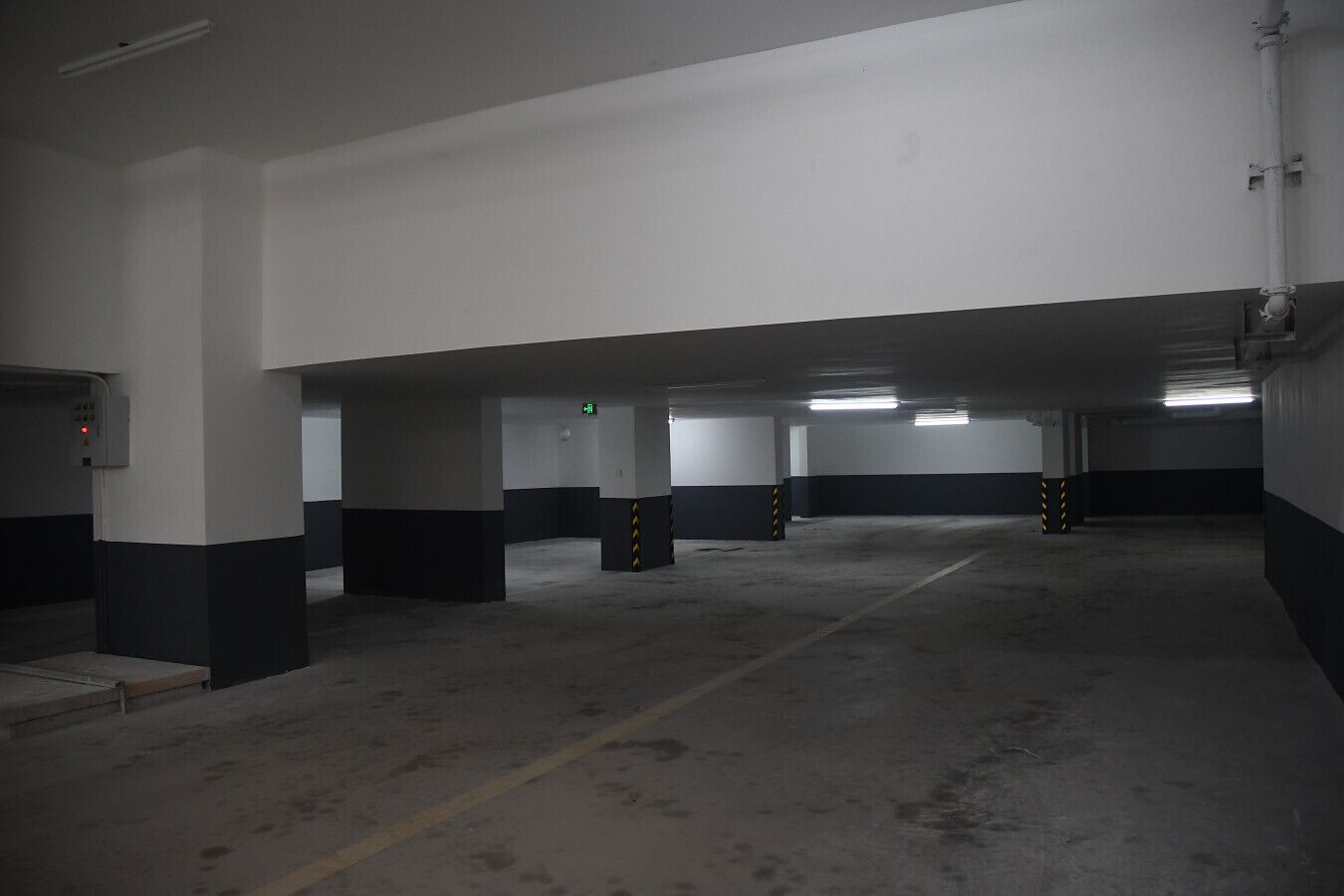 A multi-level parking garage with concrete floors and pillars, emergency exit signs, and fluorescent lighting.