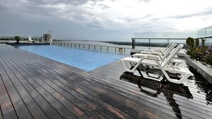 Piscina no terraço com espreguiçadeiras e vista para o horizonte da cidade.