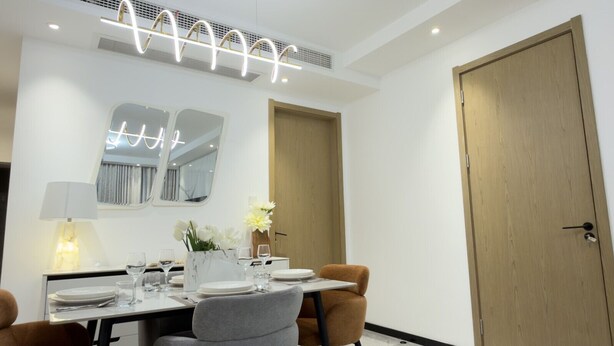 Uma sala de jantar moderna, com uma mesa posta para quatro pessoas, um espelho acima da mesa e uma porta de madeira à direita.